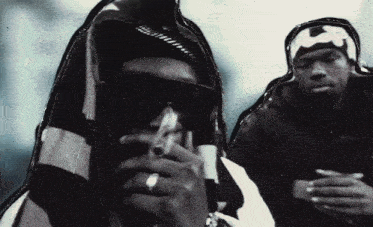 a black and white photo of a man smoking a cigarette and another man with a bandana on his head
