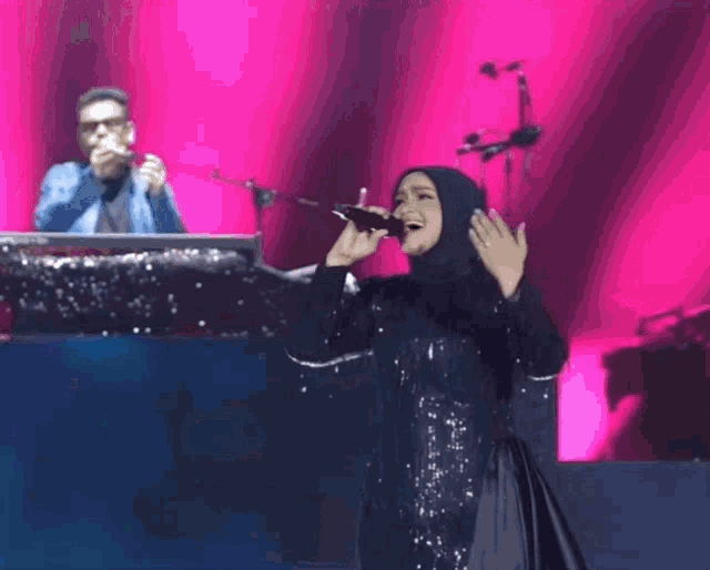 a woman in a hijab sings into a microphone on stage