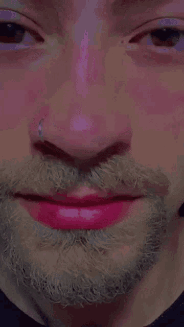 a man with a beard and a nose ring has pink lipstick on his lips .