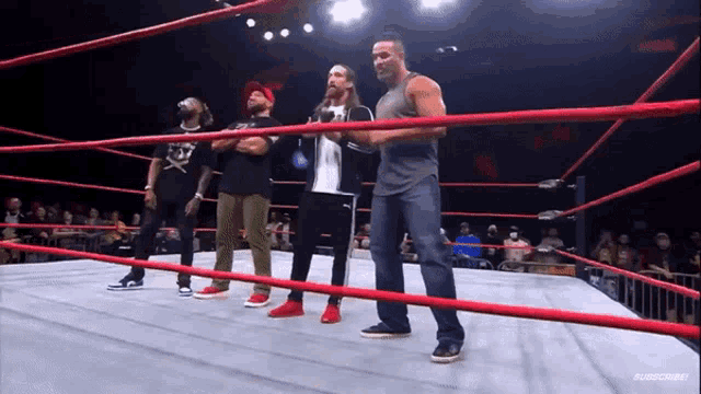 a group of men are standing in a wrestling ring with the words subscribe on the bottom left