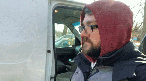 a man wearing a hooded jacket and glasses is sitting in a van