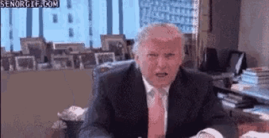 a man in a suit and tie is sitting at a desk in a room .
