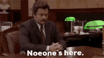 a man in a suit and tie is sitting at a desk with the words `` noone 's here '' written on it .
