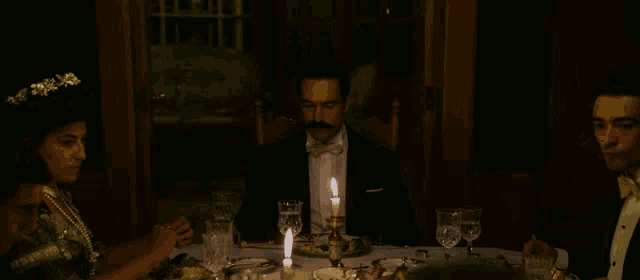 a man in a tuxedo sits at a table with a candle