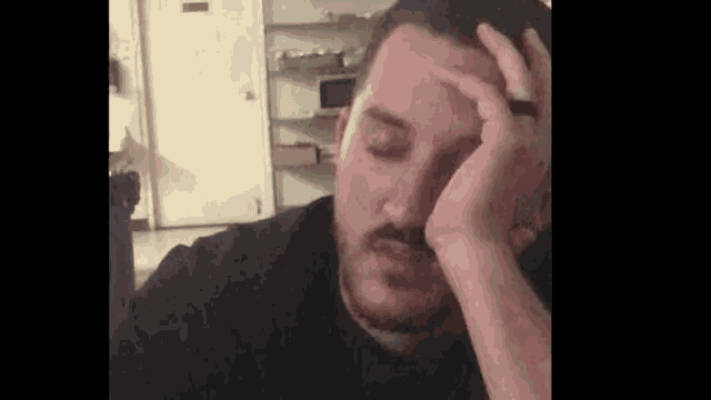 a man with a beard is holding his head with his hand .