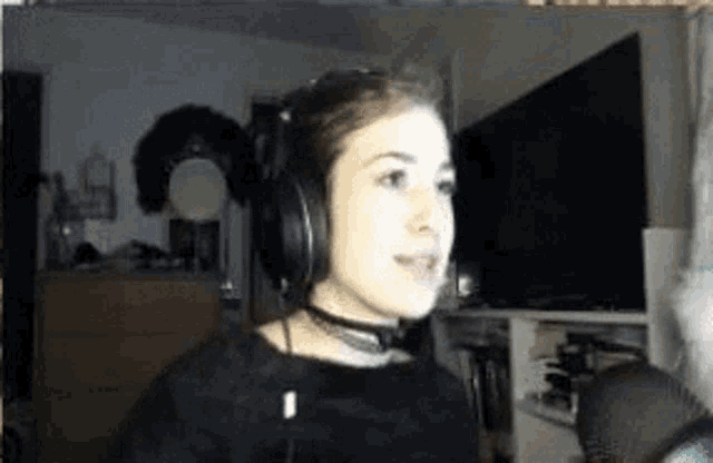 a woman wearing headphones and a choker is sitting in front of a tv .