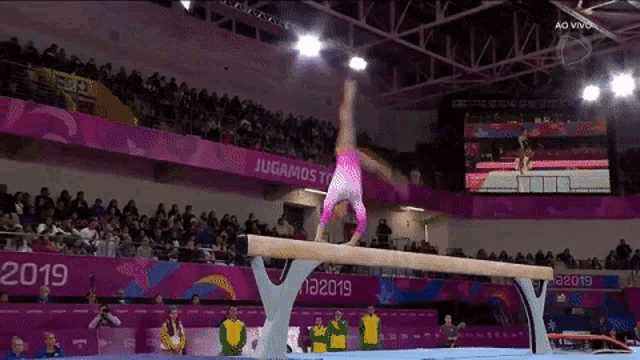 a gymnast is doing a trick on a balance beam in front of a crowd .