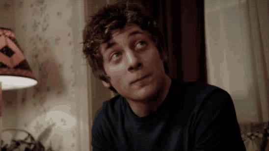 a young man with curly hair is sitting in front of a lamp looking up .