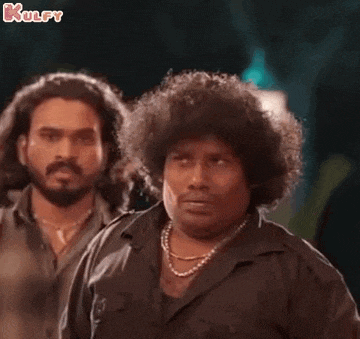 two men with curly hair are standing next to each other and one has a necklace around his neck .