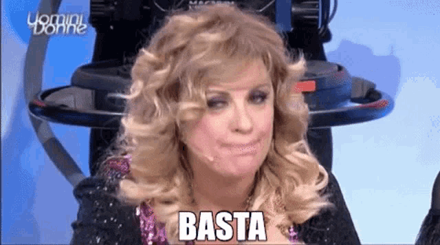 a woman with blonde hair is sitting in front of a camera and says basta