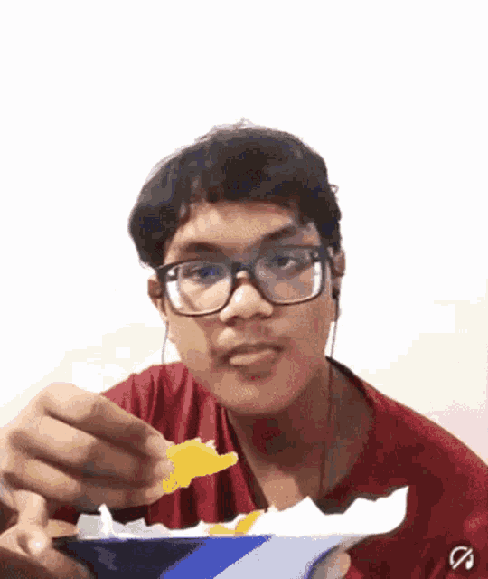 a young man wearing glasses is eating chips from a blue container