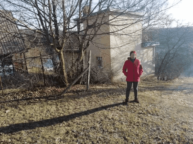 a woman in a red jacket is standing in front of a house