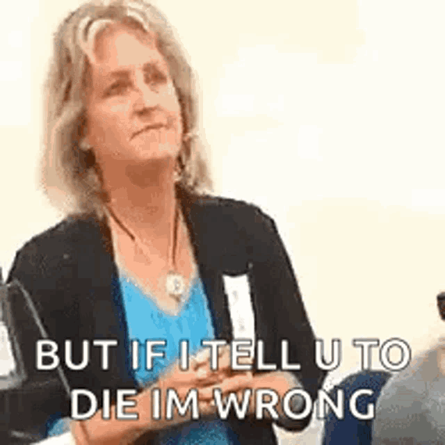 a woman in a blue shirt and black jacket is sitting in a chair and talking to someone .