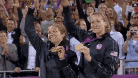 two female athletes are holding up their medals in front of a crowd
