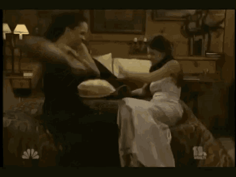 two women are fighting with pillows in a bedroom .