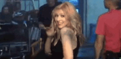 a woman in a black dress is smiling and dancing in a room with other people .