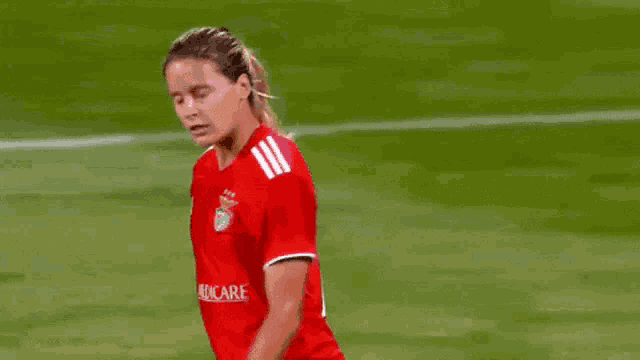 a female soccer player in a red jersey is walking on a field .