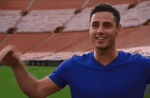 a man in a blue shirt is standing on a soccer field and smiling .