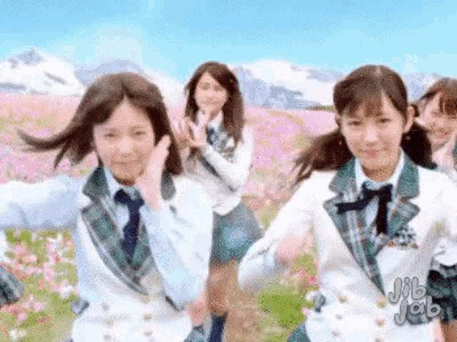 a group of young women in school uniforms are dancing in a field of flowers .