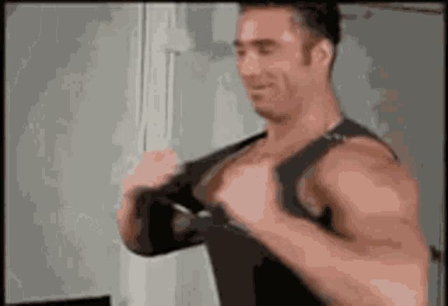 a muscular man is wearing a black tank top and adjusting his bra .