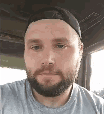 a man with a beard is wearing a baseball cap and a grey shirt .