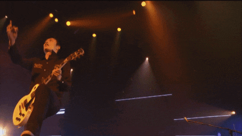 a man playing a guitar in front of a large screen that says d