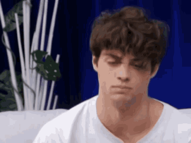 a young man with curly hair is sitting on a couch and making a face .