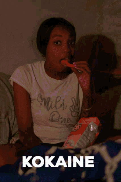 a woman is sitting on a couch eating a candy bar and the word cocaine is above her