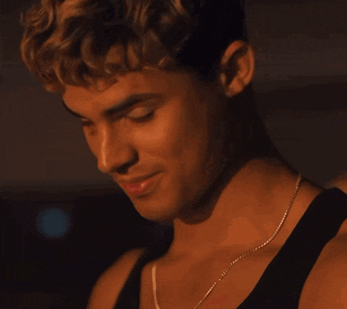 a close up of a man wearing a black tank top and a necklace