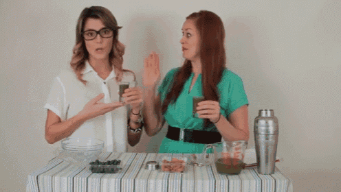 two women sitting at a table holding glasses of green juice