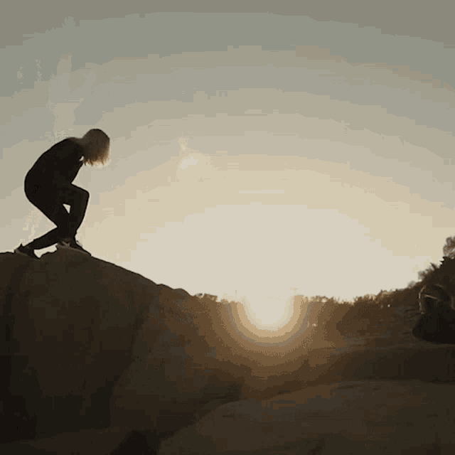 a silhouette of a person standing on top of a rock with the sun behind them
