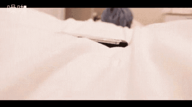 a person with blue hair laying on a bed with a remote control