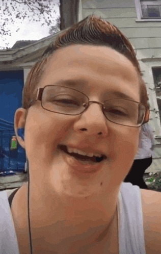 a woman wearing glasses and a white tank top smiles
