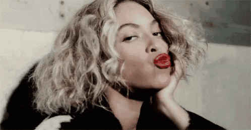 a woman with curly hair and red lips is blowing a kiss .
