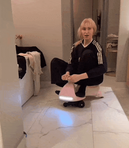 a woman in a black adidas shirt sits on a pink toy