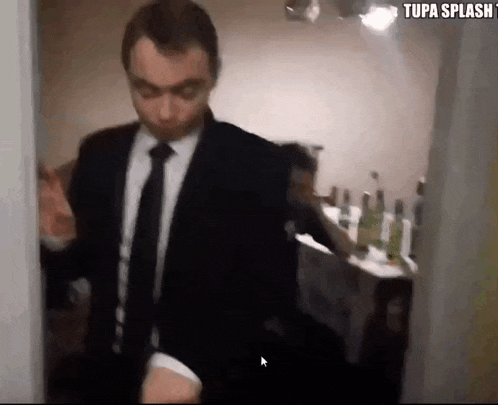 a man in a suit and tie is walking through a doorway with the words tupa splash on the bottom right