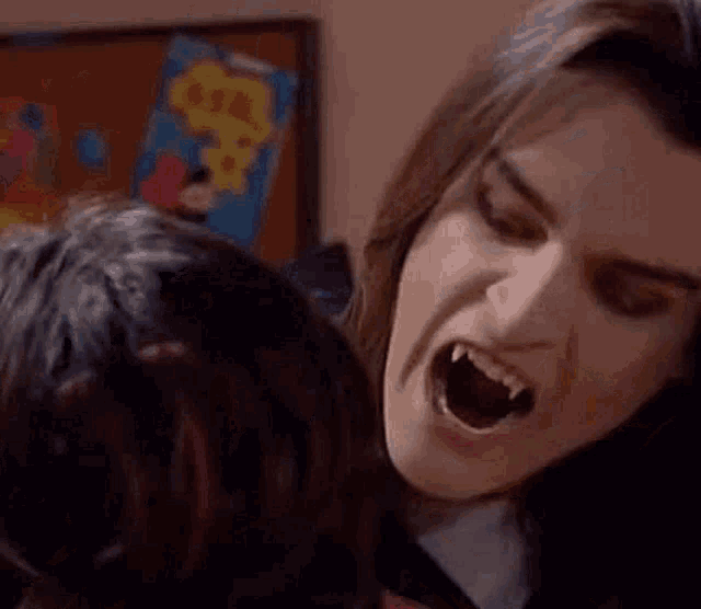 a close up of a woman with vampire teeth screaming at another woman .