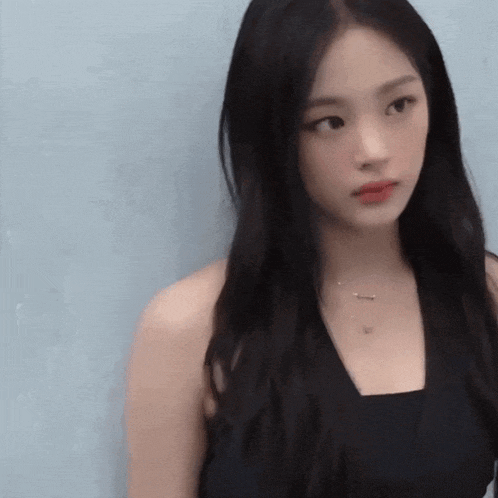a woman with long black hair wearing a black tank top and a necklace
