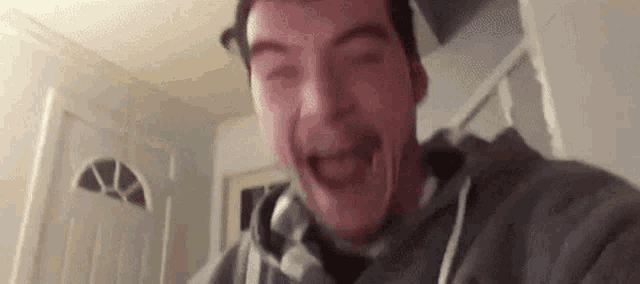 a man in a gray hoodie is making a funny face while looking at the camera .