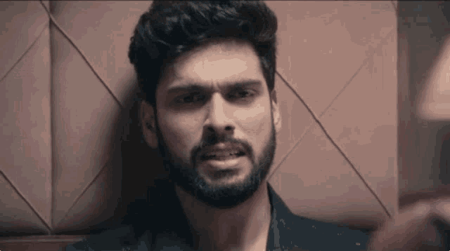 a man with a beard is leaning against a wall making a funny face .