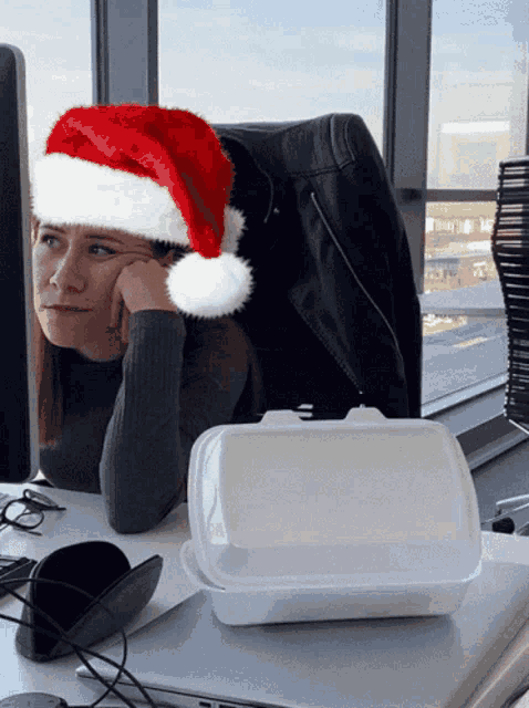 a woman wearing a santa hat sits at her desk