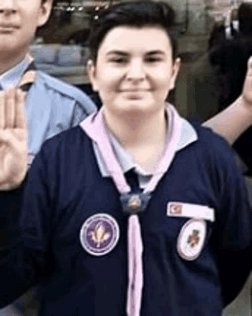 a girl scout wearing a pink sash and a blue shirt is giving a thumbs up .