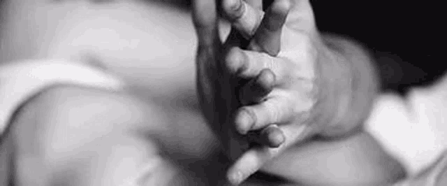 a black and white photo of a person holding the hand of a baby .