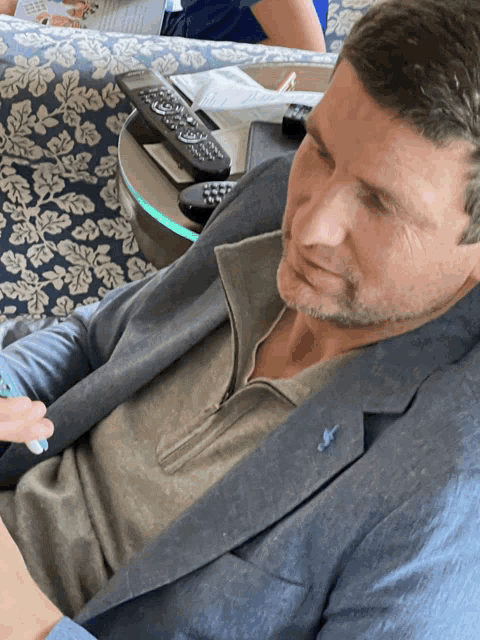a man in a suit sits on a couch next to a table with remote controls on it