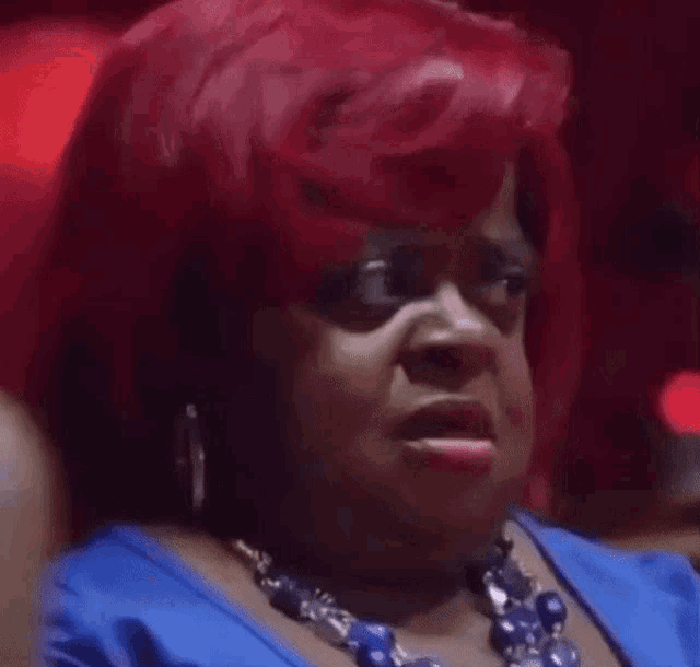 a woman with red hair and a blue necklace is making a face .