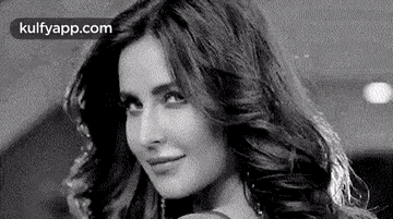 a black and white photo of a woman with long wavy hair smiling .