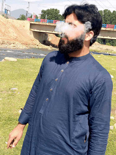 a man in a blue shirt is smoking a cigarette in front of a river