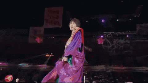 a man in a purple outfit stands on a stage with a sign that says i 'm your girl