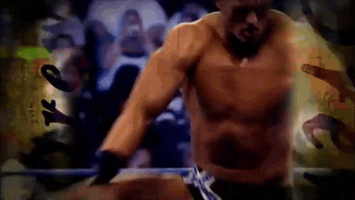 a man without a shirt is standing in a boxing ring surrounded by people .