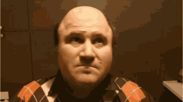 a bald man wearing an orange and black plaid shirt